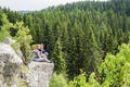 A man and a woman sit hugging each other on the edge of a mountain in nature