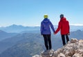 Man and woman stand holding hands on the edge of a cliff overlooking the mountains Royalty Free Stock Photo