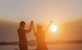 The man and woman standing holding hands at the sea watching the sunset