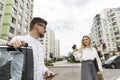 Man and woman are standing together outside on the street. Guy s leaning on car`s door. He is holding phone in hands. Girls is Royalty Free Stock Photo