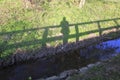 Man or woman stands on a bridge, their shadow falls on a meadow on banks of a stream Royalty Free Stock Photo