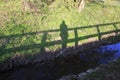 Man or woman stands on a bridge, their shadow falls on a meadow on banks of a stream Royalty Free Stock Photo