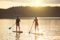 Man and woman sup board surfers at sunset. Royalty Free Stock Photo