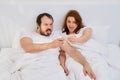 A man and a woman take a selfie photo funny in a white bed. Husband and wife spend time at home under the coronavirus quarantine