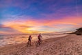 Man and woman together riding bicycle on sand beach romantic sky at sunset. Real people getting away from it all. Dramatic clouds Royalty Free Stock Photo