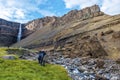 Man and woman tourists enjoying spectacular landscape around of Hengifoss waterfall and basaltic strata with thin, red and yellow