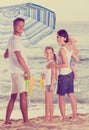 man and woman with two kids standing together under beach umbrel