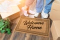 Man and Woman Unpacking Near Welcome Home Welcome Mat, Moving Boxes and Plant