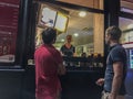 Man and woman wait for their snack while shop employee prepares their snack on a Paris evening.