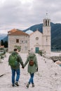 Man and woman walk holding hands towards the Church of Our Lady of the Rocks. Back view. Montenegro