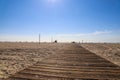 A man and a woman walking down a wooden boardwalk in the sand at the beach with people relaxing on the beach Royalty Free Stock Photo