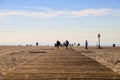 A man and a woman walking down a wooden boardwalk in the sand at the beach with people relaxing on the beach Royalty Free Stock Photo