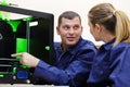 man and woman wearing overalls using 3d printer