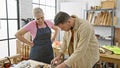 A man and woman work together in a carpentry workshop surrounded by wood, tools, and workbench Royalty Free Stock Photo