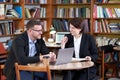 Man and woman working with laptop sitting in modern stylish room with bookshelves on background in library or bookstore Royalty Free Stock Photo
