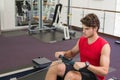 Adult man pulling foam handle on rower at gym wearing red sleeveless shirt wristwatch, copy space Royalty Free Stock Photo