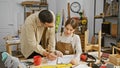 A man and woman in a workshop collaborate over a document surrounded by woodworking tools and materials Royalty Free Stock Photo