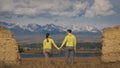 Man and woman in yellow green sportswear. Lovely couple of travelers hug and kiss near old stone enjoying highland Royalty Free Stock Photo