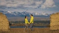 Man and woman in yellow green sportswear. Lovely couple of travelers hug and kiss near old stone enjoying highland Royalty Free Stock Photo