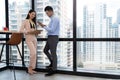 Man and woman businesss team standing beside the windows and discussing in the modern high level building. Man looking at tablet