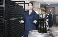 man and women coworkers looking at bubbly wine in bottle standing in wine cellar