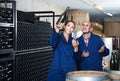 man and women coworkers looking at bubbly wine in bottle standing in wine cellar