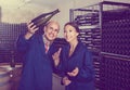 man and women coworkers looking at bubbly wine in bottle standing in wine cellar