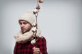 Man in a woolen scarf and hat is holding a cotton branch on grey background with copy space Royalty Free Stock Photo