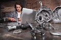 Man work with caliper measure the motor gear, study on the computer and search in internet spare engine parts on the workbench in Royalty Free Stock Photo