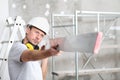 Man work, checks the straightedge to level the wall, with ladder and scaffolding in the interior construction site on background