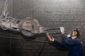 A man in work clothes and a respirator, controls heavy equipment with grinding stone to clean reinforced concrete structures in a