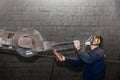 A man in work clothes and a respirator, controls heavy equipment with grinding stone to clean reinforced concrete structures in a