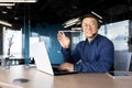 Man at work with headset phone and laptop successful asian man smiling and looking at camera at workplace inside office Royalty Free Stock Photo