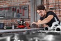 Man work in home workshop garage with sandpaper sanding surface of metal pipe on the workbench full of wrenches, diy and craft