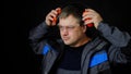 A man in work overalls puts on noise-canceling ear protectors, earmuffs on a black background.