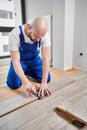 Male worker drawing line on laminate wood plank in apartment.