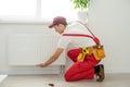 Man in work overalls using wrench while installing heating radiator in room. Young plumber installing heating system in