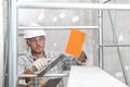 Man work, professional construction worker with plastering tools on scaffolding, safety hard hat, gloves and protective glasses.