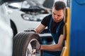 Man in work uniform sitting and changing car wheel indoors. Conception of automobile service Royalty Free Stock Photo