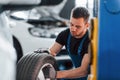 Man in work uniform sitting and changing car wheel indoors. Conception of automobile service Royalty Free Stock Photo