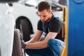 Man in work uniform sitting and changing car wheel indoors. Conception of automobile service Royalty Free Stock Photo