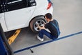 Man in work uniform sitting and changing car wheel indoors. Conception of automobile service Royalty Free Stock Photo