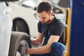 Man in work uniform sitting and changing car wheel indoors. Conception of automobile service Royalty Free Stock Photo