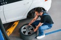 Man in work uniform sitting and changing car wheel indoors. Conception of automobile service Royalty Free Stock Photo