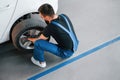 Man in work uniform sitting and changing car wheel indoors. Conception of automobile service Royalty Free Stock Photo