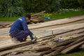 Man worker in blue work clothes handles wooden planks with grinding machine on background of green bushes and lawn Royalty Free Stock Photo