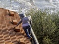 A man worker is cleaning a clogged roof gutter from dirt, debris and fallen leaves to prevent water and let rainwater drain