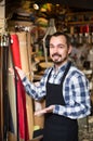 Man worker displaying various belts in leather workshop