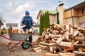 A man worker loads firewood into a wheelbarrow for heating the house,