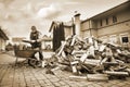 A man worker loads firewood into a wheelbarrow for heating the house,